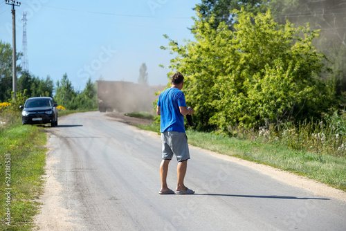 A man with a camera is walking along the road. View from the back.
