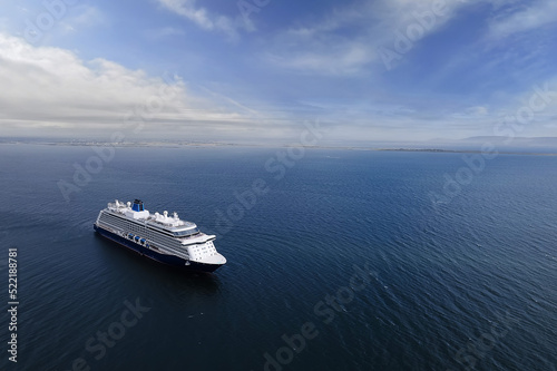 Cruise ship in the ocean. Blue cloudy sky. Tourism and travel concept. Elegant voyage by water. Aerial view. Calm water surface. Copy space. Calm and peaceful mood.