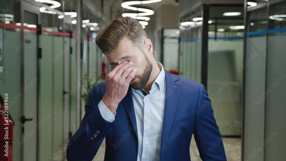 Portrait of sad overwhelmed businessman in formal suit standing at office corridor, suffering from bad news. Stressed male manager overworked in office. Portrait of sad overwhelmed businessman in formal suit standing at office corridor, suffering from bad news. Stressed male manager overworked in office.