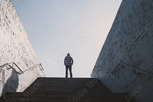 A man stands against the sky at the top of the stone stairs of the underground passage subway back view. Man conquered addiction and gained freedom. Religious and social content. Raise your hands