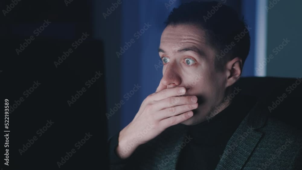 Afraid and shocked man looking at monitor screen, takes off glasses and cover his mouth with his hand while working at computer laptop late at night. Male scared of bad news, read terrible message. Afraid and shocked man looking at monitor screen, takes off glasses and cover his mouth with his hand while working at computer laptop late at night. Male scared of bad news, read terrible message.