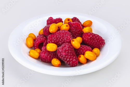 Large ripe raspberries and sea buckthorn lie in a white saucer