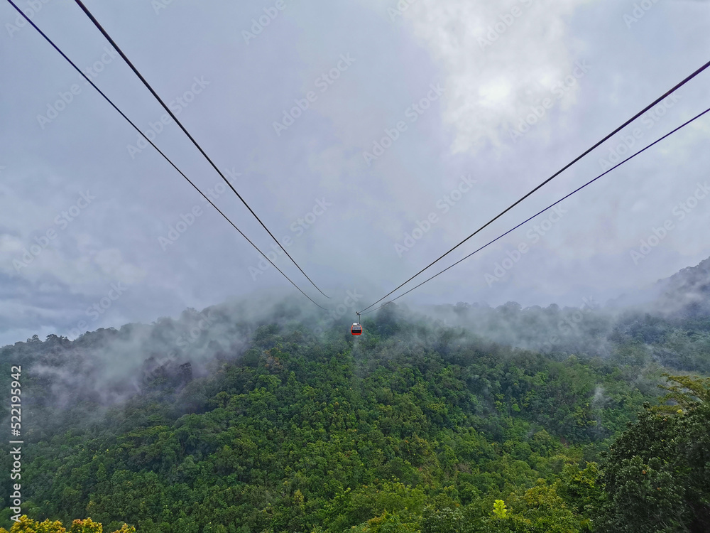 Bright red cable car with double safety sling to the cloudy misty forest in highland mountain in rainy day