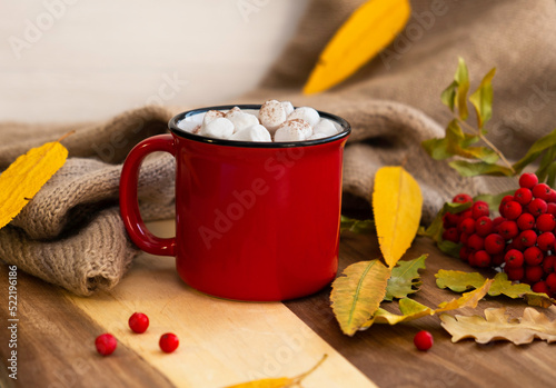 Red mug of cocoa, yellow leaves and cinnamon, on a light background. Autumn concept