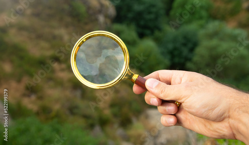 Male hand holding magnifying glass in outdoor.