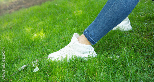 Young woman wearing stylish sneakers on green grass.