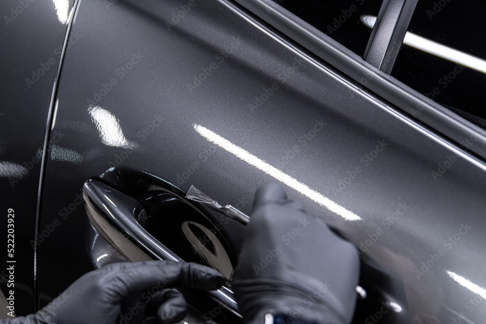 employee of the car detailing studio protects the car body with a colorless protective film