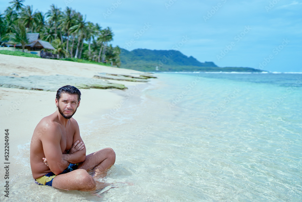 Enjoying suntan and vacation.Young bearded man ralaxing on the tropical sand beach.