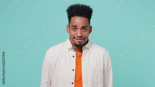 Young man of African American ethnicity wear shirt t-shirt spread hand shrugging shoulders look puzzled have no idea nothing to say I don't know why isolated on plain pastel light blue cyan background