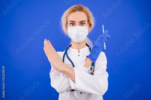 Portrait of a female doctor in a protective mask shows a gesture against vaccinations