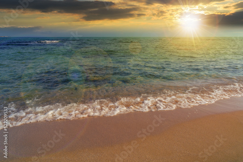 Fototapeta Naklejka Na Ścianę i Meble -  sunny sunset scenery at the sea. calm waves washing the sandy beach. transparent water and bright blue sky in evening light