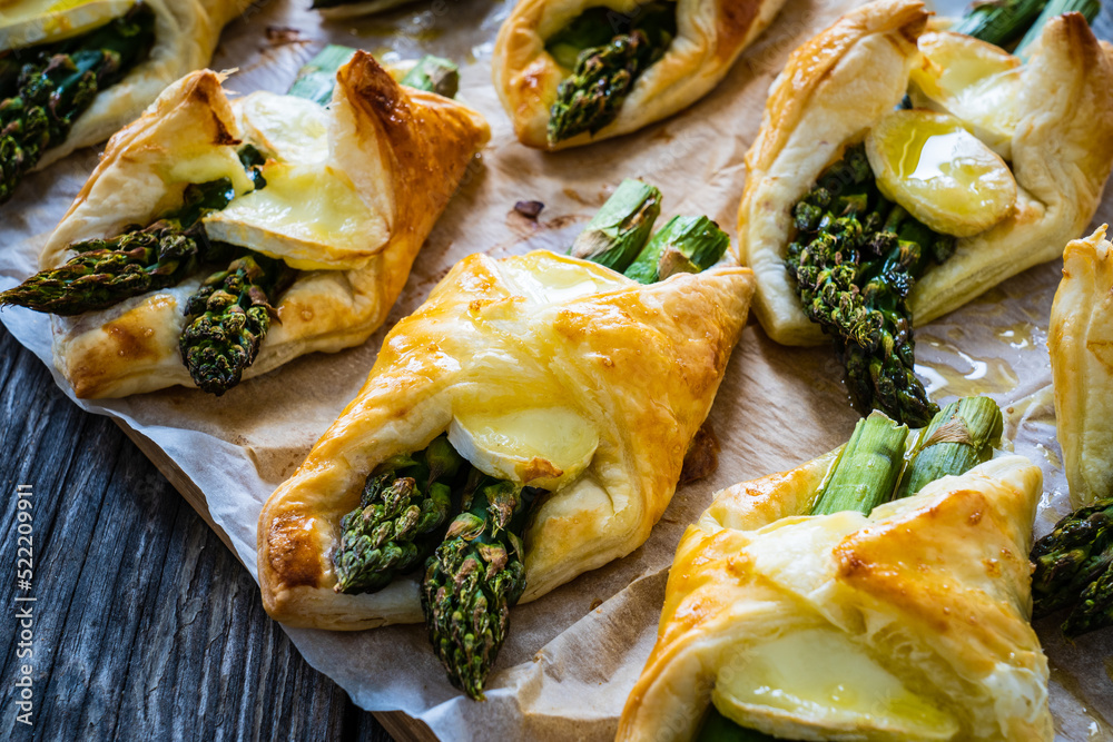 Baked puff pastry with asparagus and cheese on baking paper on wooden table - obrazy, fototapety, plakaty 