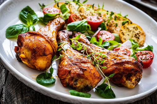 Barbecue chicken drumsticks with fried potato, lettuce and mini tomatoes on wooden table 