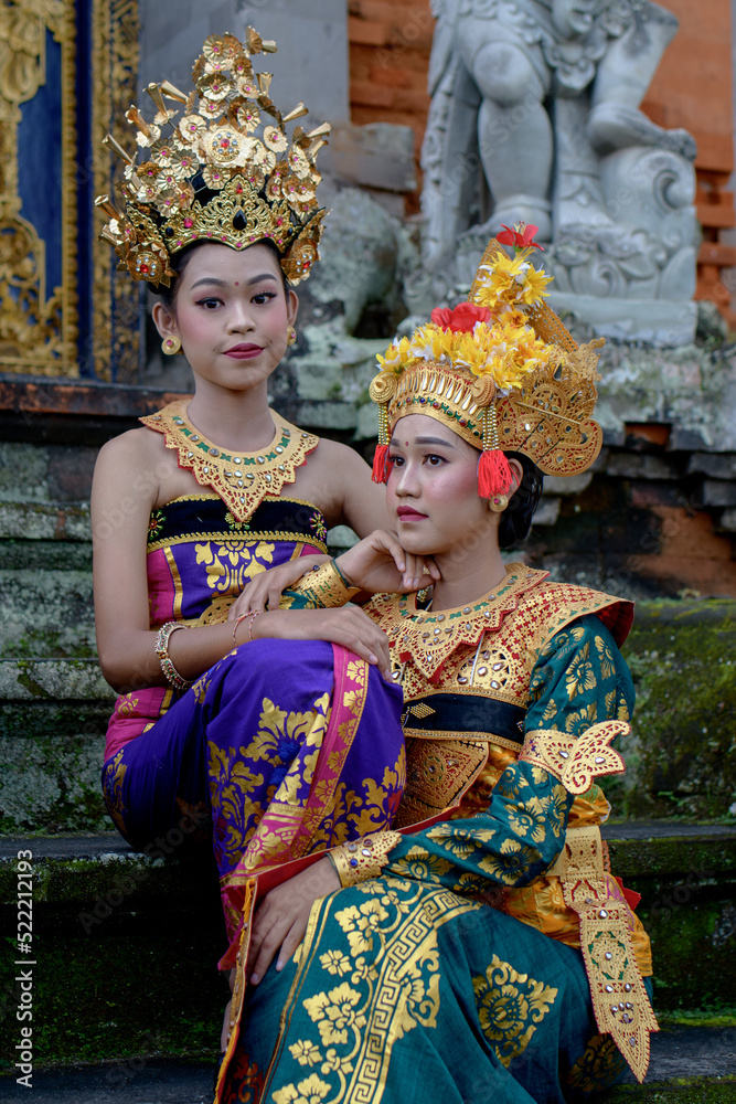 Two young Bali smiling girls make -up dressed in traditional colored costumes inside in the temple. Two young Bali smiling girls make -up dressed in traditional colored costumes inside in the temple.