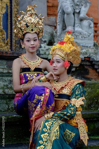 Two young Bali smiling girls make -up dressed in traditional colored costumes inside in the temple. © Ace Mason