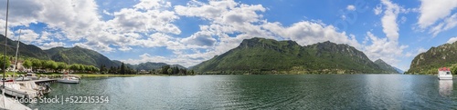 Maxi panoramic shot of glacier Lombard highland lake Idro  Lago d Idro  surrounded by alpine wooded cliffs under piercing blue sky  several boats at a pier.  Brescia  Lombardy  Italy