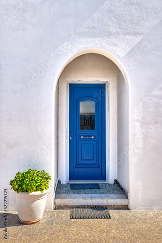 Traditional blue door and whitewashed walls of Greek house entrance and flower pot with rich foliage. Midday, summer sunshine, Milos, Greece © NPershaj