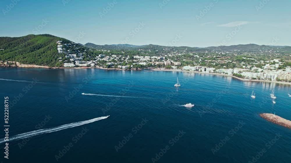 Ships floating by Santa Eulària des Riu coastal Town on a sunny day in Ibiza. Aerial view of resorts and hotels by the coast with blue transparent water on the Balearic Islands in Spain. Ships floating by Santa Eulària des Riu coastal Town on a sunny day in Ibiza. Aerial view of resorts and hotels by the coast with blue transparent water on the Balearic Islands in Spain.