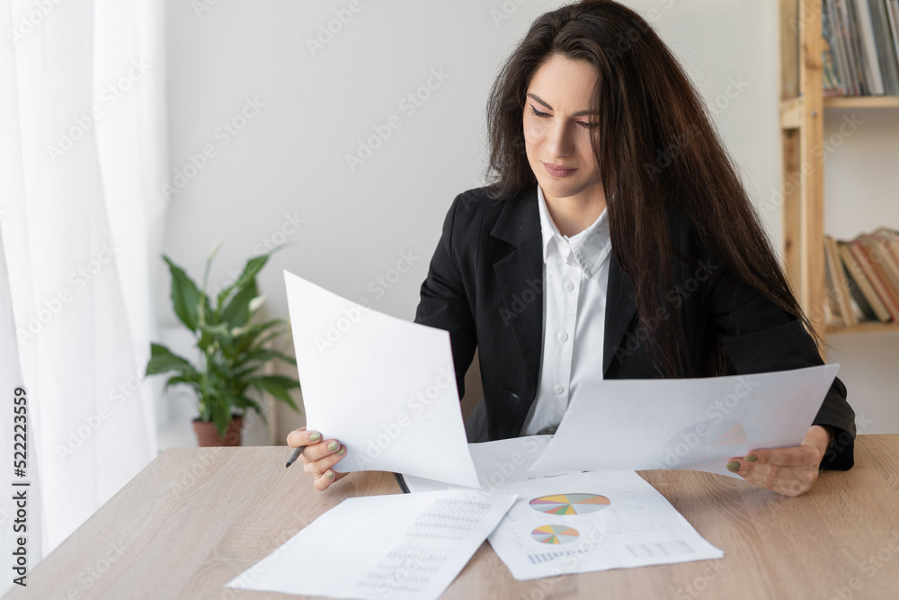 Serious latin business woman working in office with documents. Women working arrange documents with papers on the office desk Serious latin business woman working in office with documents. Women working arrange documents with papers on the office desk