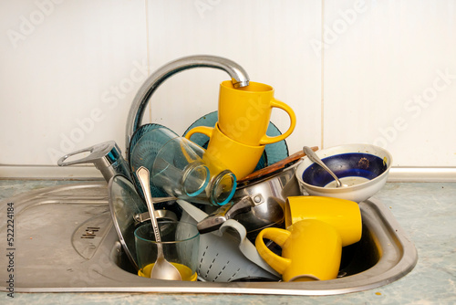 Dirty and unwashed dishes are stacked in the kitchen sink. Unwashed cups, plates, pots, forks and spoons.A mountain of untidy and used dishes.