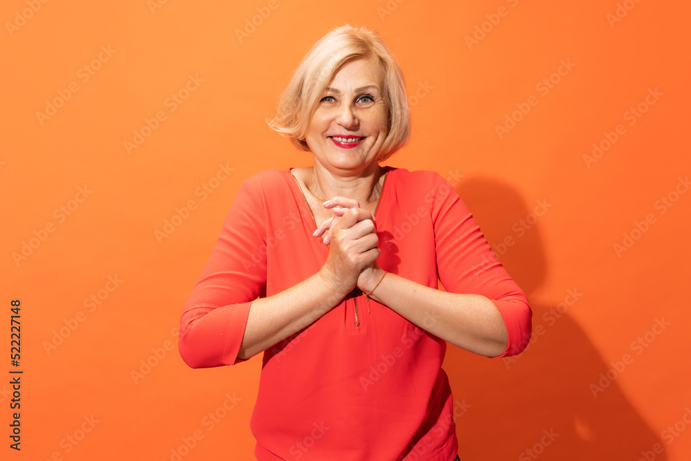 Half-length portrait of beautiful middle age woman with blond hair posing isolated on orange color background. Concept of emotions, facial expressions Half-length portrait of beautiful middle age woman with blond hair posing isolated on orange color background. Concept of emotions, facial expressions