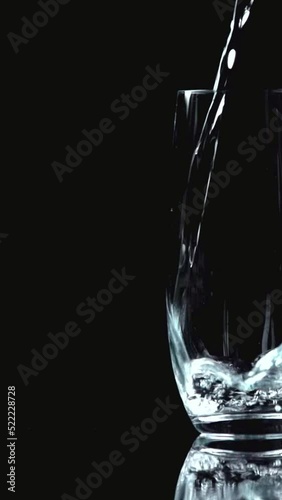 vertical video of water pouring into transparent glass isolated on black