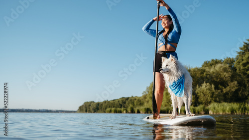 Happy Young Woman Enjoying Life on the Lake at Early Morning Standing on the Sup Board with Her Dog Snow-White Japanese Spitz