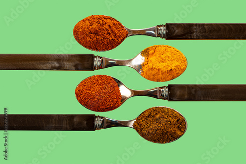 A selection of cayenne pepper tumeric chilli curry powder spices used in Indian cooking on a coulerful green background photo