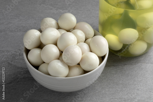 Bowl with preserved cooked Quail eggs close up and a glass jar on the background photo