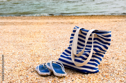 beach bag and slippers on the beach by the sea