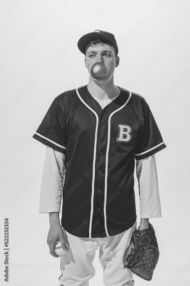 Portrait of young man, baseball player in uniform with bubblegum, in glove with ball posing. Black and white photography