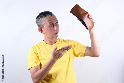 Portrait of Asian Man wearing yellow tshirt with shocked face expression showing empty wallet, cashless. 