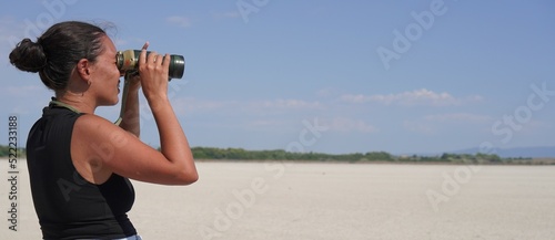 Attractive brunette woman poses in dry salty lake new goals for her future with binoculars, concept search for new goals