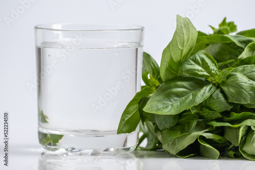 Chlorophyll extract and basil is poured in pure water in glass against a white background and green organic basil herbs. Growing fresh plants, healthy food. Concept of superfood, detox and diet photo