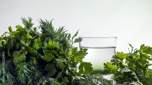 Chlorophyll extract is poured in pure water in glass against a white background and green organic dill and parsley herbs photo