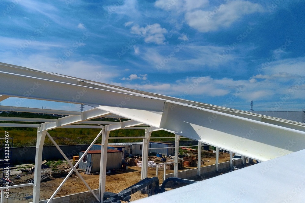 Low angle view of green metal roof of industrial building structure in construction site against blue sky background Low angle view of green metal roof of industrial building structure in construction site against blue sky background