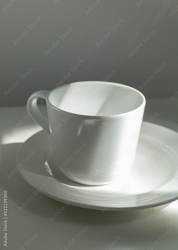 a white porcelain cup stands on a saucer in the morning sun a white porcelain cup stands on a saucer in the morning sun