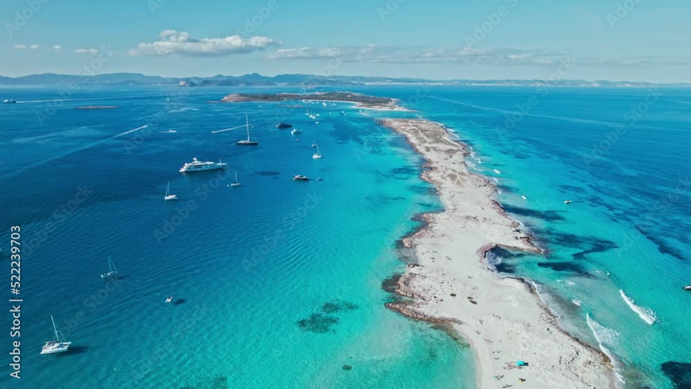 White sand Platja de Ses Illetes Beach on a narrow strip of land on Formentera. Blue famous beach with people relaxing on vacation in the mediterranean sea with luxury vessels and boats.