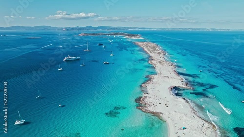 White sand Platja de Ses Illetes Beach on a narrow strip of land on Formentera. Blue famous beach with people relaxing on vacation in the mediterranean sea with luxury vessels and boats.