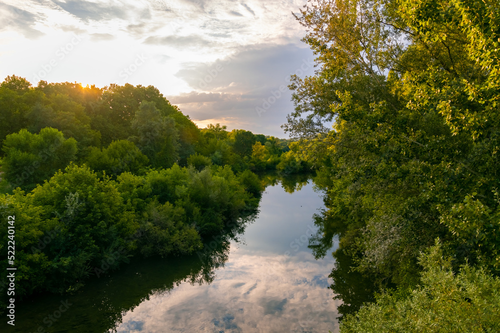 River panorama on a sunny summer evening in romantic Cèze valley in La Roque sur Cèze in Provence south France. Sunset twilight and cloudy sky reflected by calm water surface. Trees on the riverbanks River panorama on a sunny summer evening in romantic Cèze valley in La Roque sur Cèze in Provence south France. Sunset twilight and cloudy sky reflected by calm water surface. Trees on the riverbanks