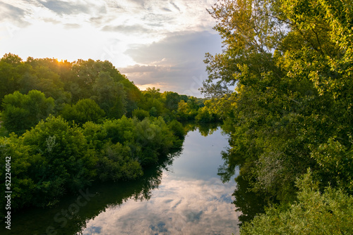 River panorama on a sunny summer evening in romantic Cèze valley in La Roque sur Cèze in Provence south France. Sunset twilight and cloudy sky reflected by calm water surface. Trees on the riverbanks