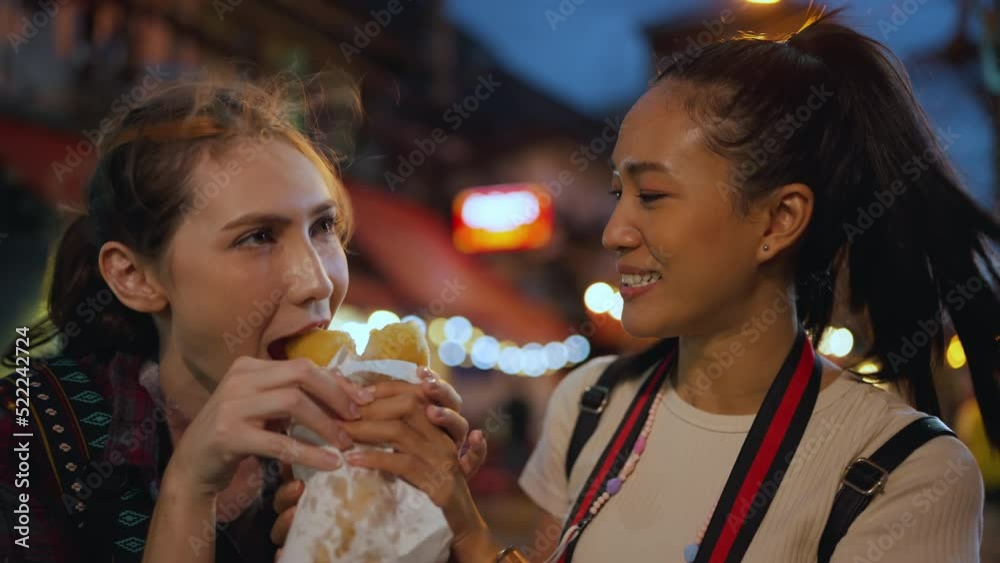 Female traveler traveling at city in the night time. They eating street food together with smiling.