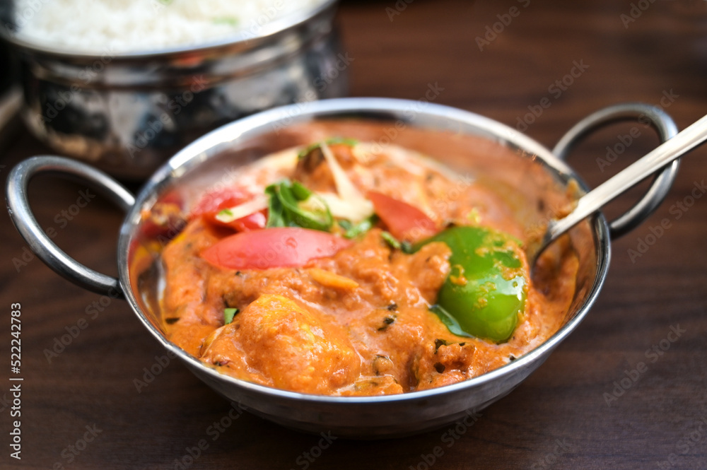 Indian chicken curry dish with vegetables in a steel bowl served with rice on a dark brown wooden table, copy space, selected focus,