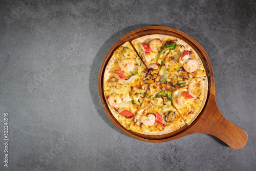 Top view of tasty hot baked seafood crispy pizza - mussels, shrimps and kani with chili pepper and melted mozzarella cheese on round pizza dough, on a wooden pizza pan over concrete texture.
