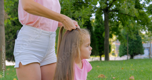 Mother making hairstyle french braid her daughter outdoor