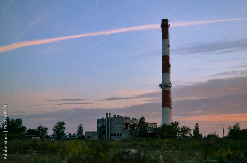 Tall chimney of a boiler house against the backdrop of a beautiful morning sky and clouds