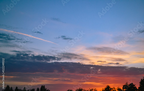 Fototapeta Naklejka Na Ścianę i Meble -  Morning glow illuminates the clouds on a beautiful colorful sky above the silhouettes of trees at dawn