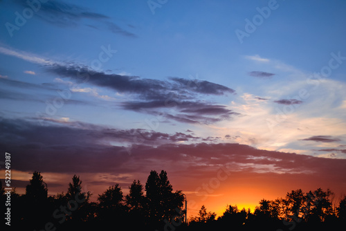The morning glow illuminates the clouds on a beautiful colorful sky above the silhouettes of trees and a pillar at dawn