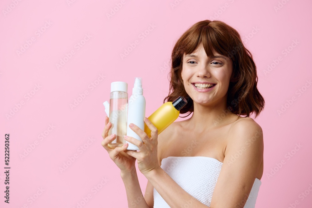 a sweet, joyful woman stands on a pink background and holds different colored jars with care products in her hands. Horizontal photography in the studio a sweet, joyful woman stands on a pink background and holds different colored jars with care products in her hands. Horizontal photography in the studio