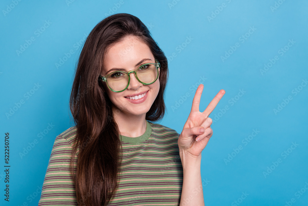 Photo of cool young brunette lady show v-sign wear eyewear green t-shirt isolated on blue background Photo of cool young brunette lady show v-sign wear eyewear green t-shirt isolated on blue background